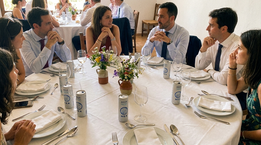 Comida de boda en el campo español con invitados y latas NEA blancas en la mesa, fotografía documental natural